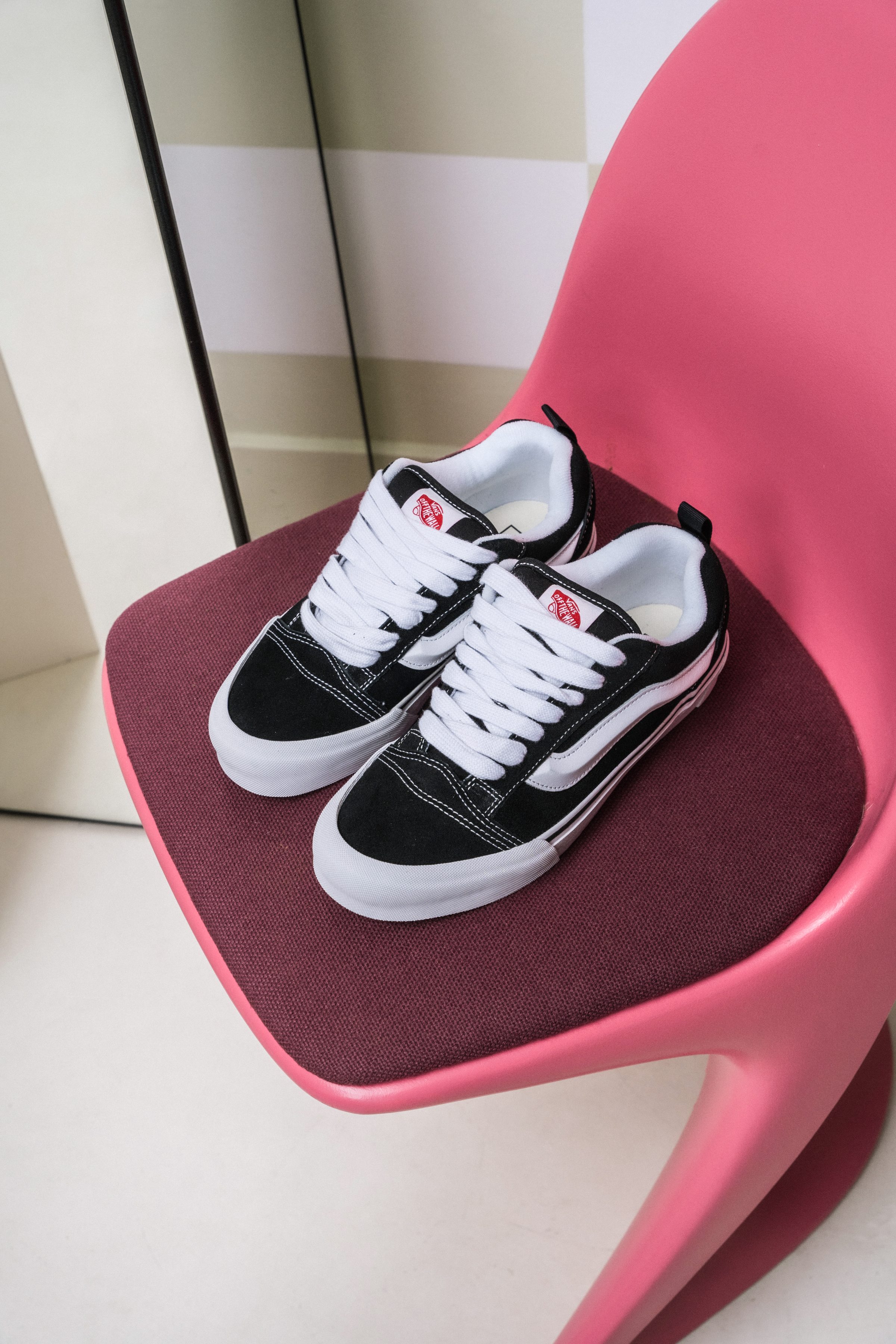 vans sneakers on a pink design chair against a checkered wall